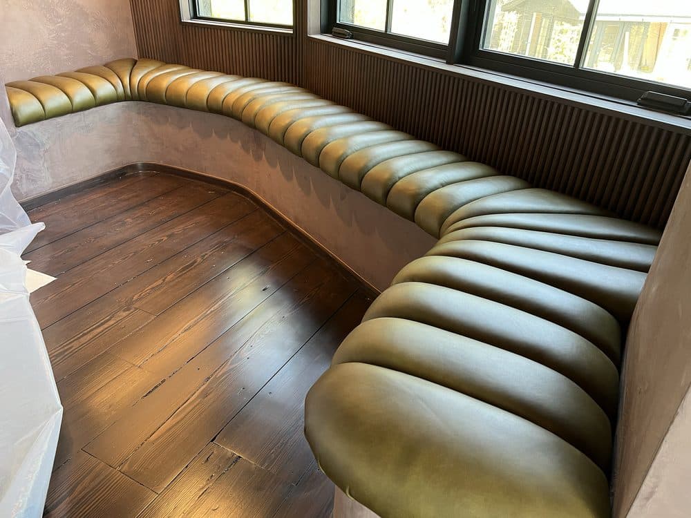 Long curved olive leather channel-tufted banquette beneath a row of windows