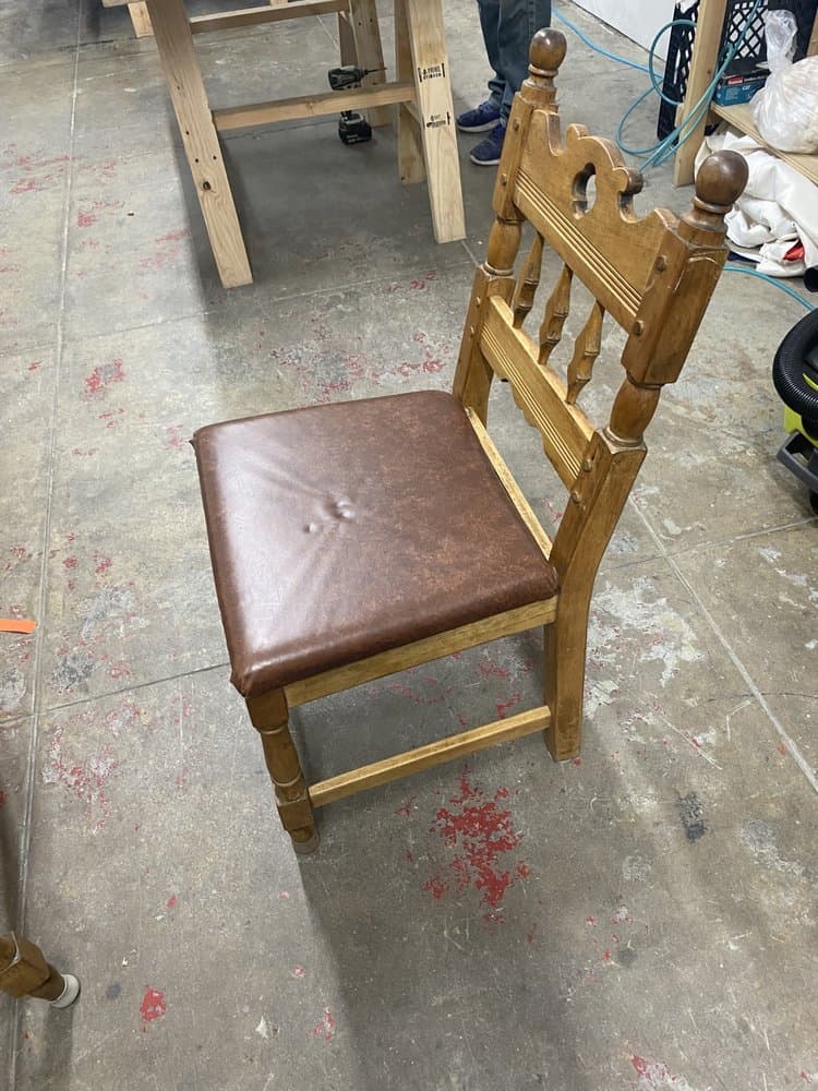 Carved wood dining chair with a recovered brown leather seat