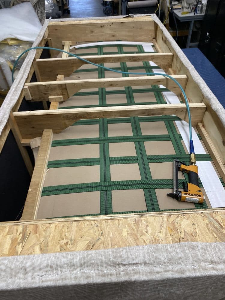 Wood sofa frame with new green elastic webbing being built in the workshop