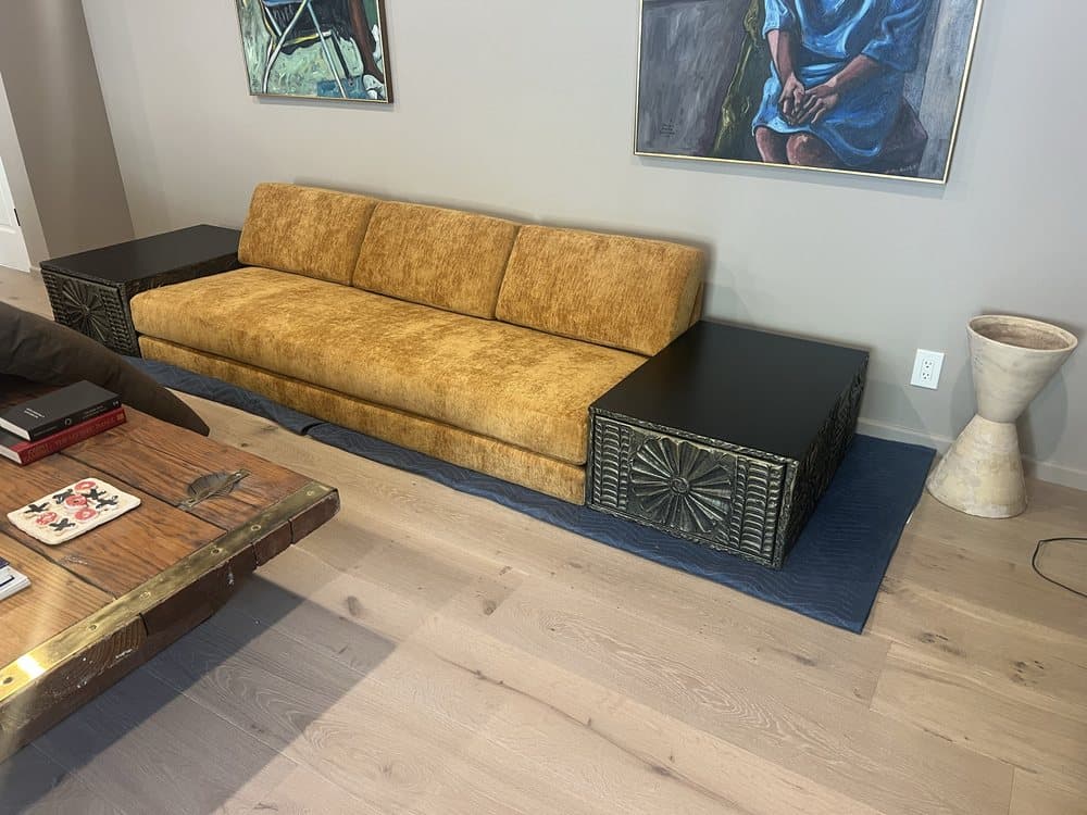 Low gold velvet sofa with three back cushions between sculpted black side tables